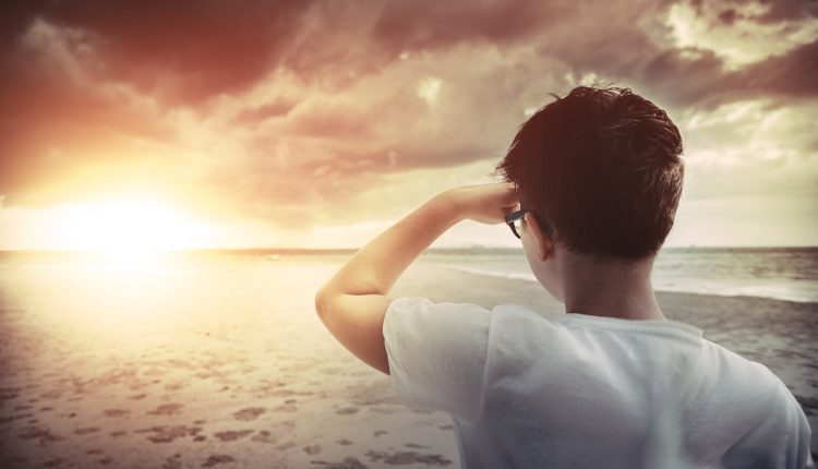 Boy standing on the beach at sunset and looking forward